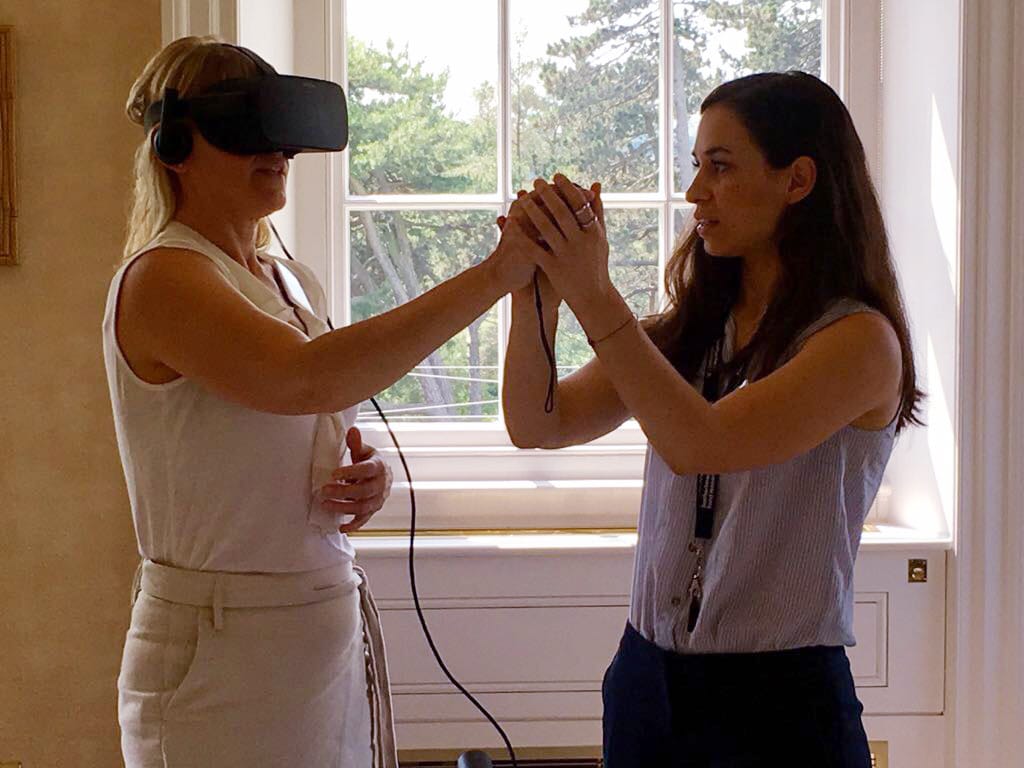 Woman wearing VR headset, being helped by second woman.
