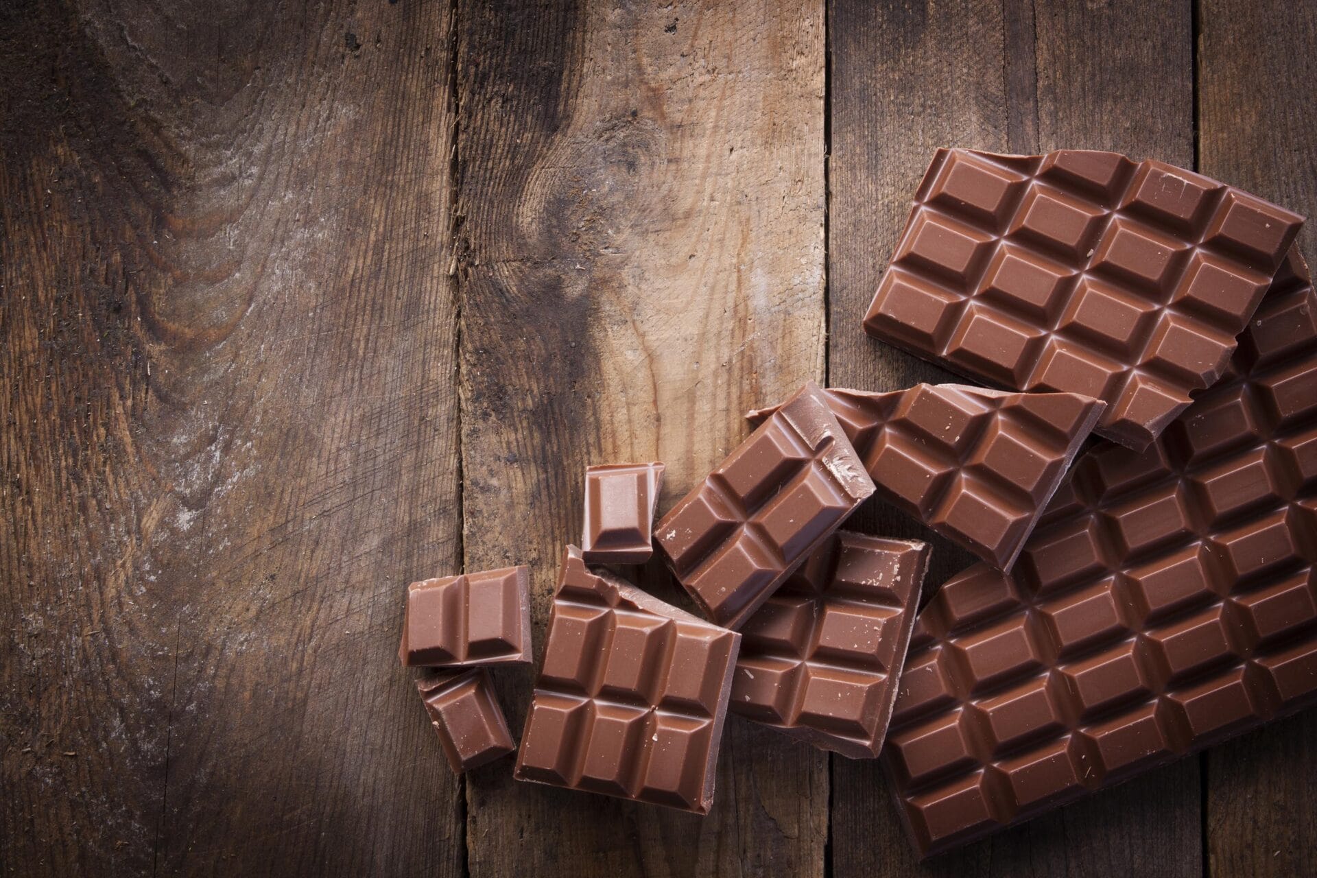 An arrangement of broken milk chocolate blocks, shot overhead on a rustic worn wooden background, using natural daylight.