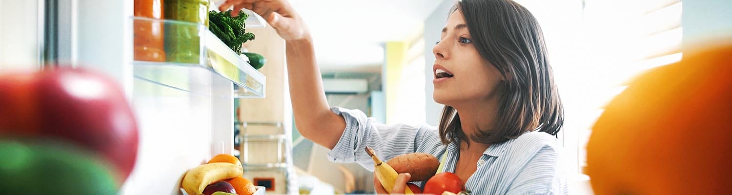 Closeup of a cheerful young couple picking some fruit and veggies from the fridge to make some healthy breakfast on Sunday morning. Shot from inside the working fridge.
